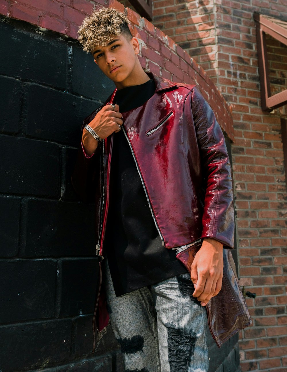 woman in red leather jacket and gray denim jeans standing beside black brick wall