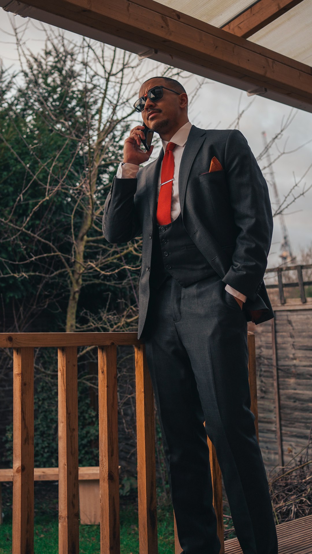 man in black suit jacket and black pants standing on brown wooden bridge during daytime