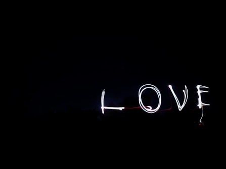 The word 'LOVE' is written in light against a dark background, likely using a long-exposure photography technique. The letters are illuminated and stand out in contrast to the black space around them.
