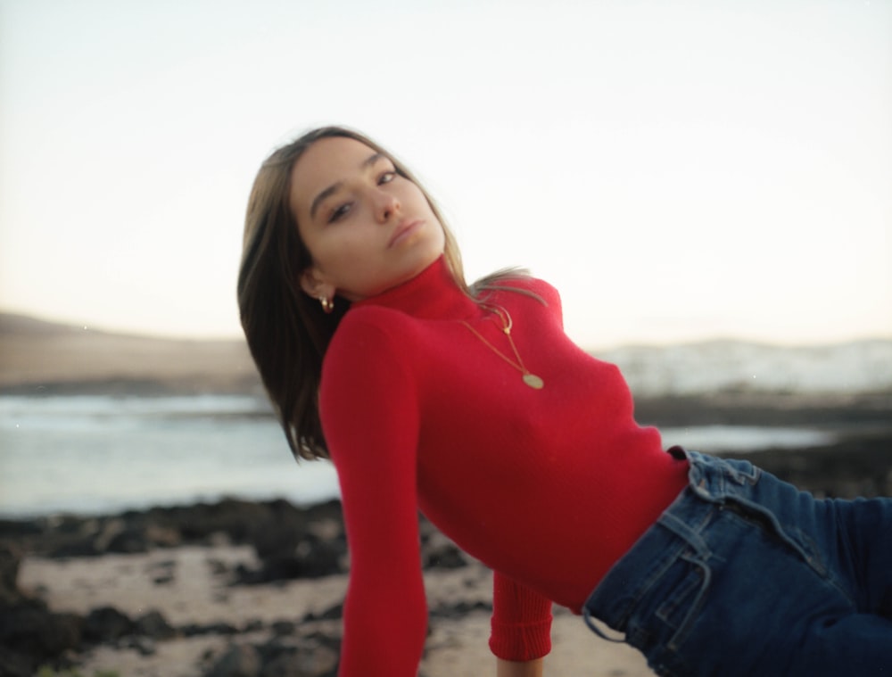woman in red long sleeve shirt and blue denim shorts standing on beach during daytime