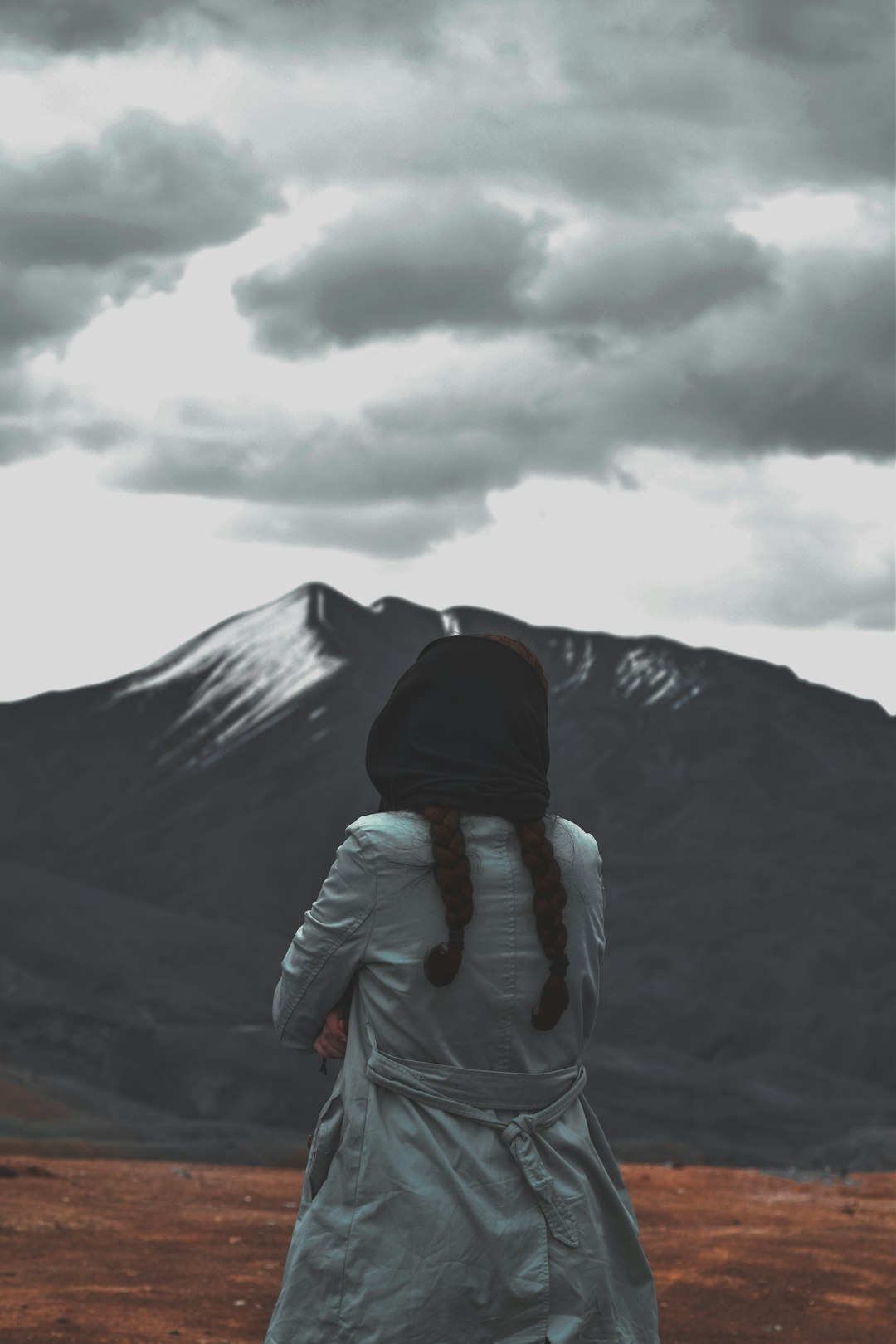 person in gray hoodie standing on mountain under gray cloudy sky during daytime