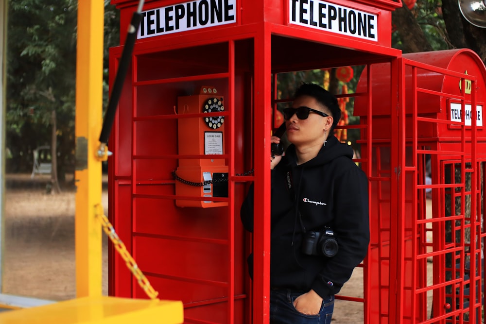 woman in black jacket wearing black sunglasses standing beside red telephone booth