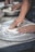 Hands are seen pressing and shaping dough on a floured surface, possibly part of a baking or pizza preparation process. A metal bowl in the background contains more dough, indicating ongoing food preparation.
