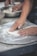Hands are seen pressing and shaping dough on a floured surface, possibly part of a baking or pizza preparation process. A metal bowl in the background contains more dough, indicating ongoing food preparation.