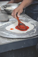 Close-up of a chef carefully spreading sauce on a handmade pizza dough in a rustic kitchen.