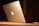 A sleek silver laptop with a glowing logo on its lid, placed on a wooden surface. The lighting is warm and subdued, creating a cozy ambiance.