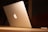 A sleek silver laptop with a glowing logo on its lid, placed on a wooden surface. The lighting is warm and subdued, creating a cozy ambiance.