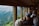 A group of people are sitting inside a train carriage, looking out the large windows at a scenic view of a mountainous landscape. Some individuals are taking photos or gazing at the view, indicating a sightseeing experience. The interior of the train has wooden paneling and a cozy atmosphere.