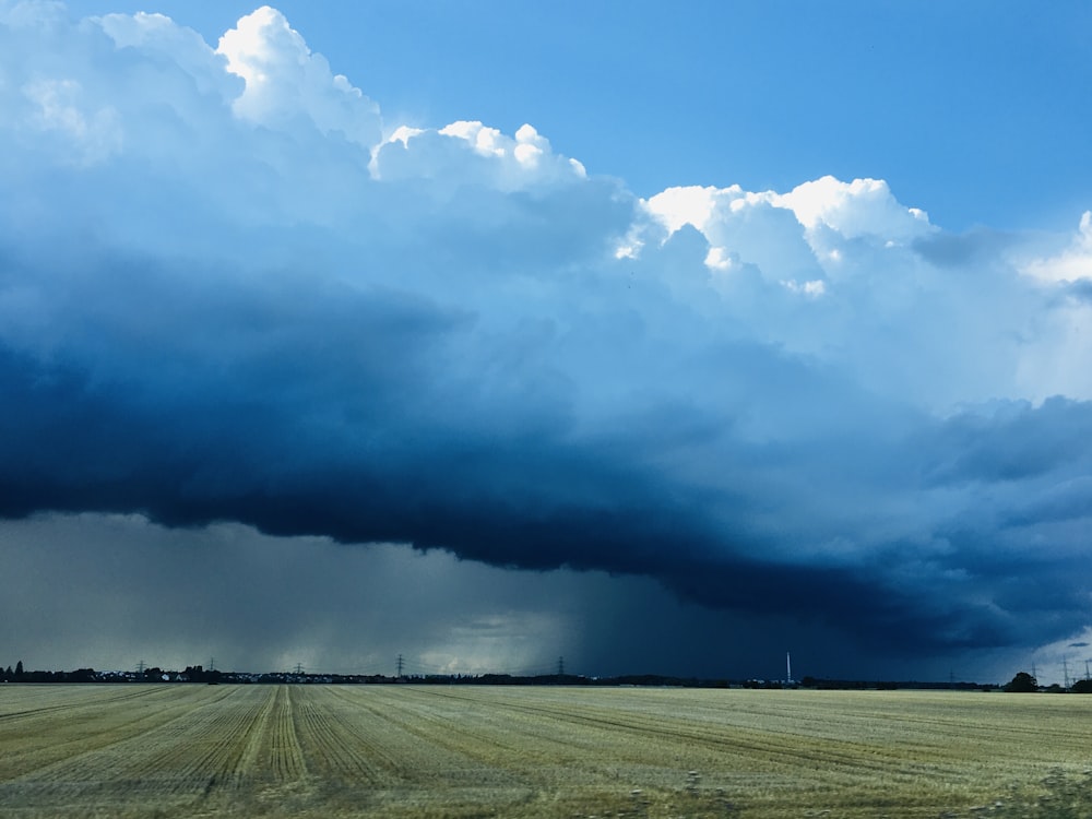 brown field under white clouds and blue sky during daytime