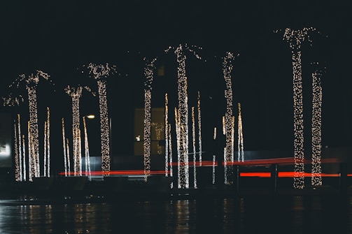 A cozy outdoor evening scene with softly glowing Christmas lights and palm trees decorated with wreaths and Santa hats.