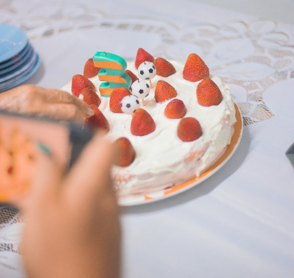 person holding white and red round cake