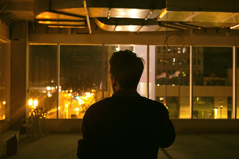 man in black jacket standing near glass window