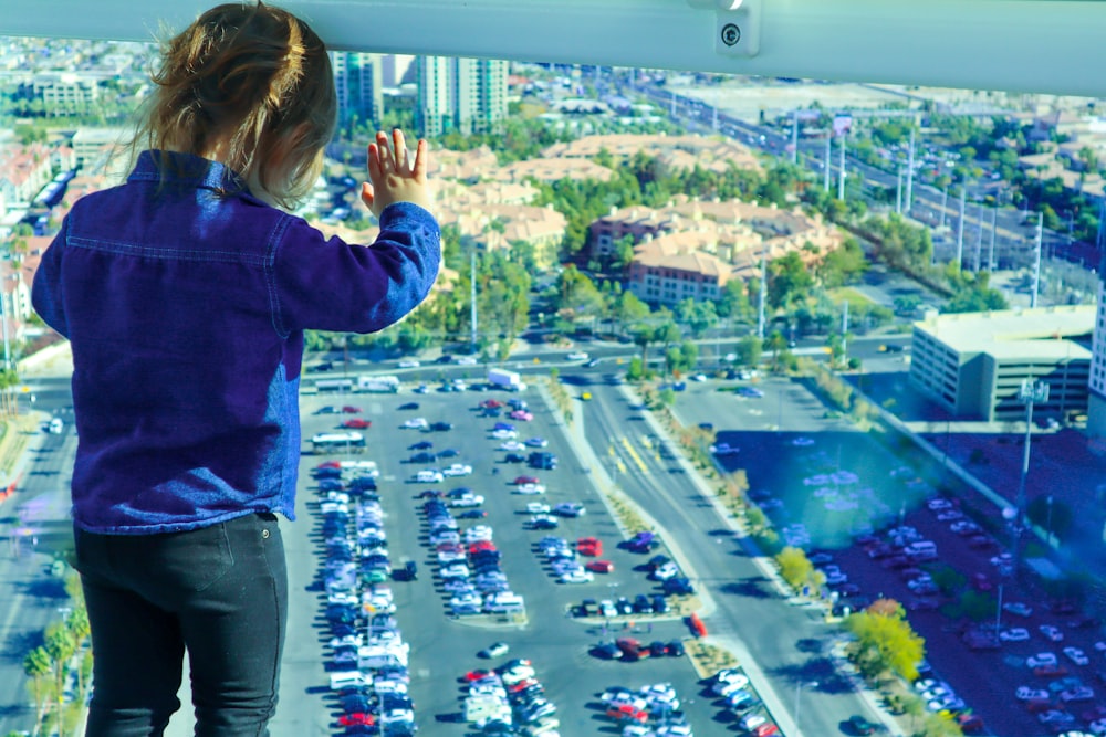 girl in blue jacket standing on top of building looking at the city