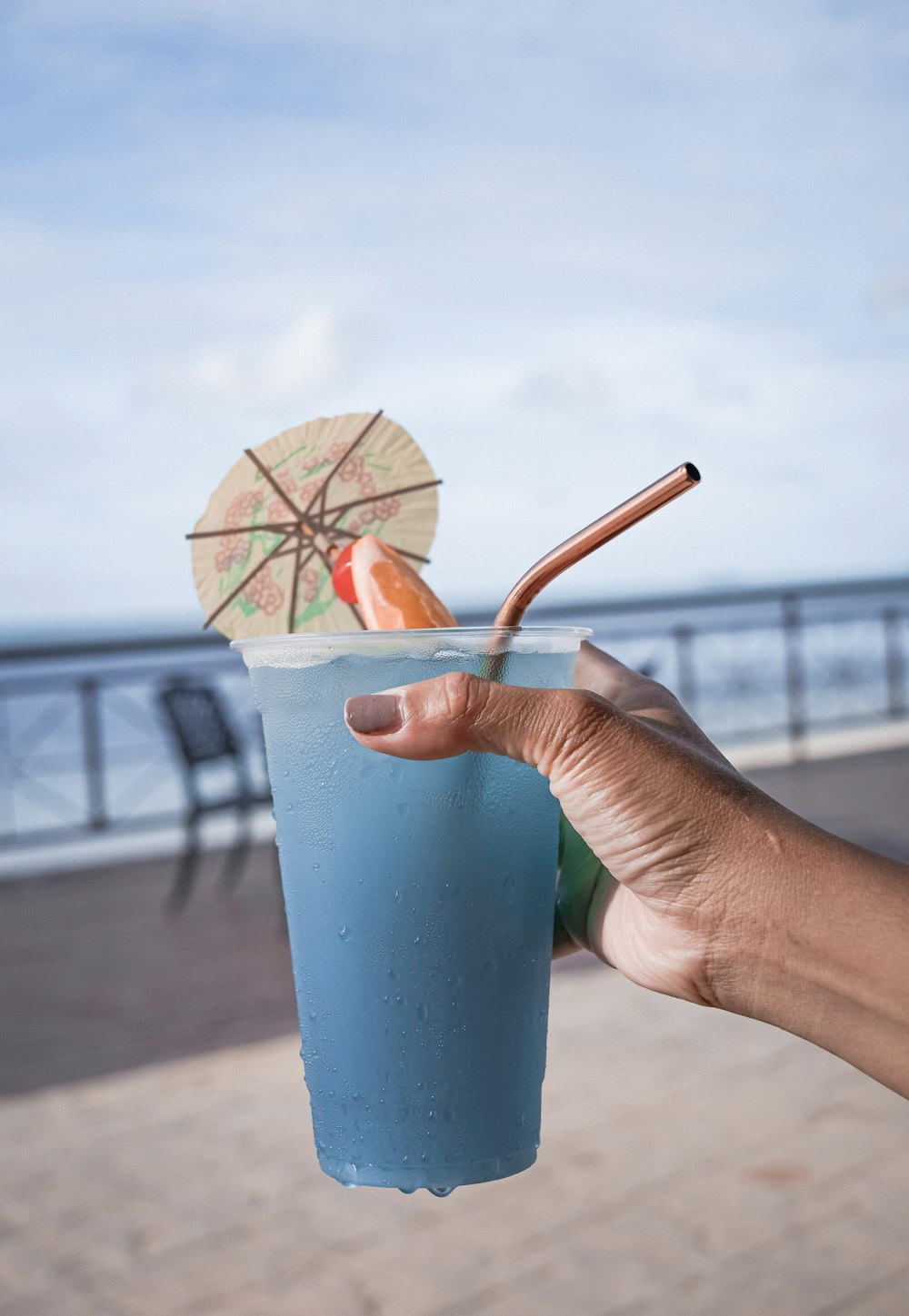 Persona sosteniendo vaso de plástico azul con paraguas marrón y rojo