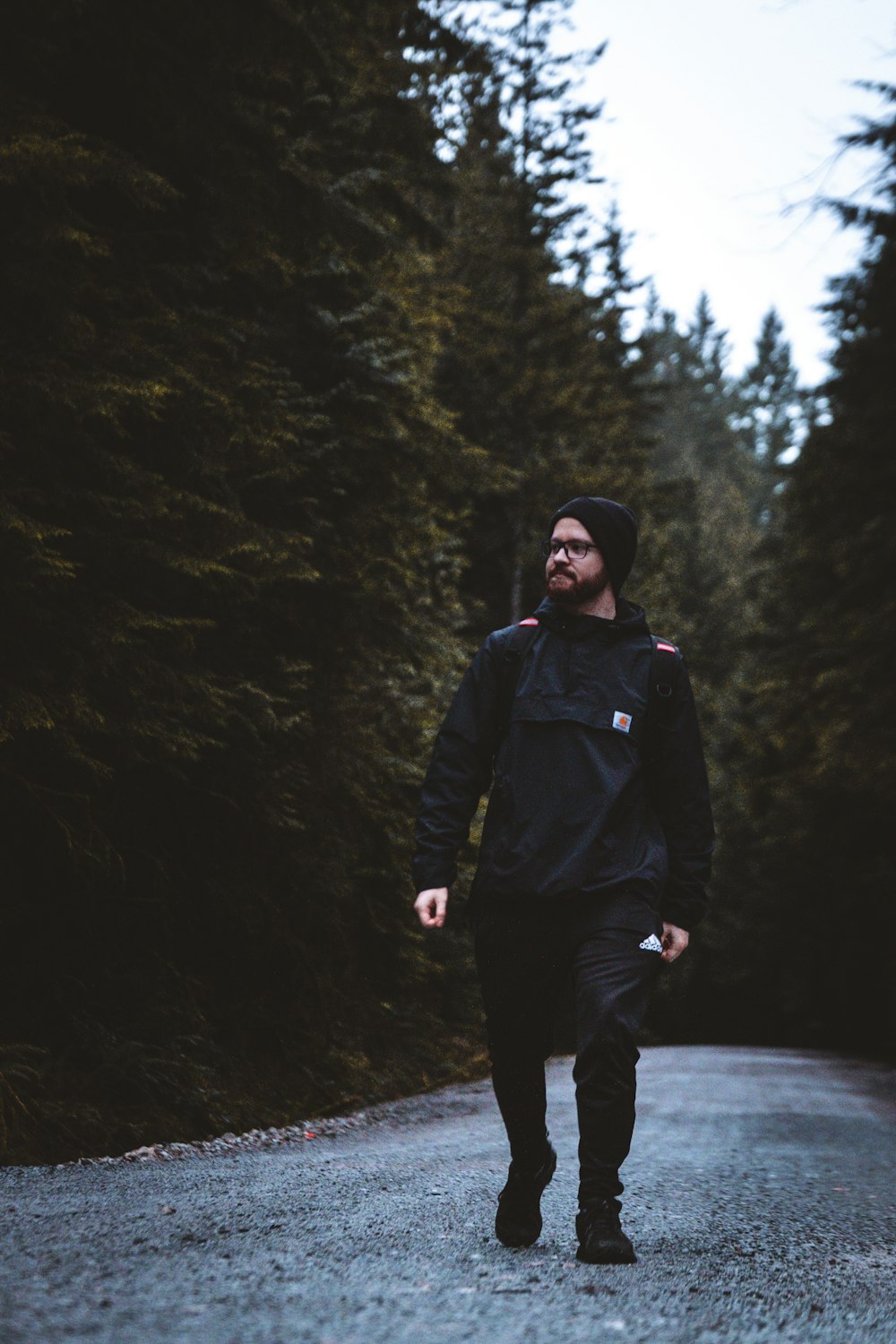 man in black jacket and black pants standing on road between trees during daytime