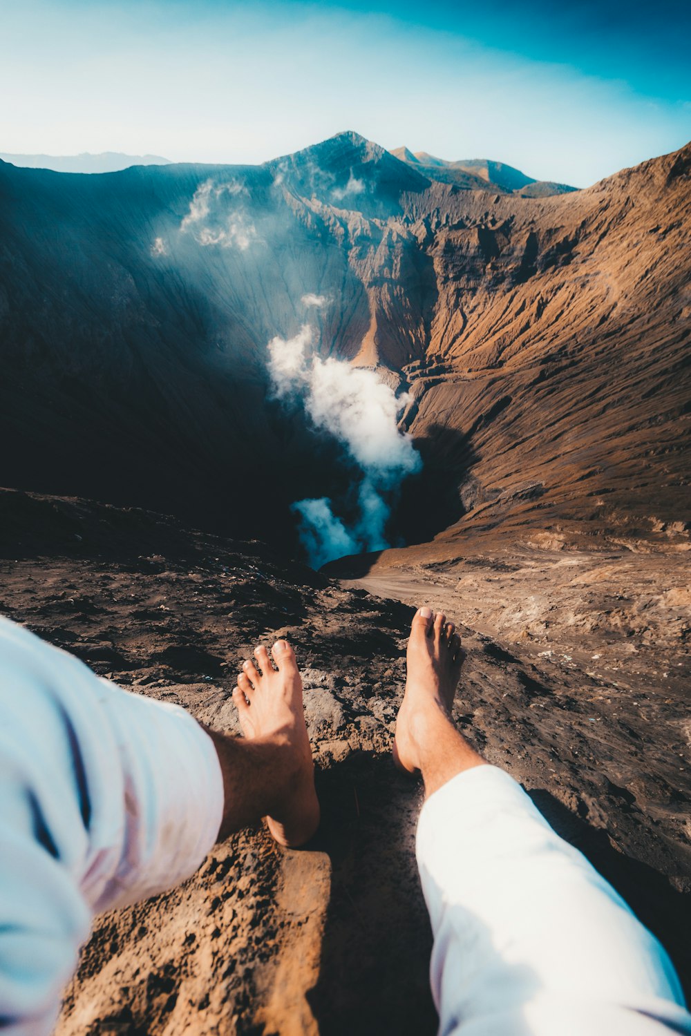 person in white pants sitting on brown rock formation during daytime