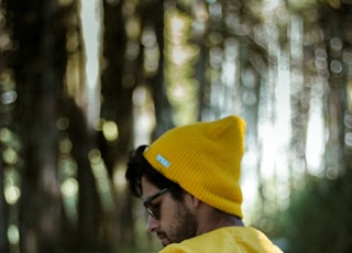 man in yellow hoodie and black knit cap standing in forest during daytime