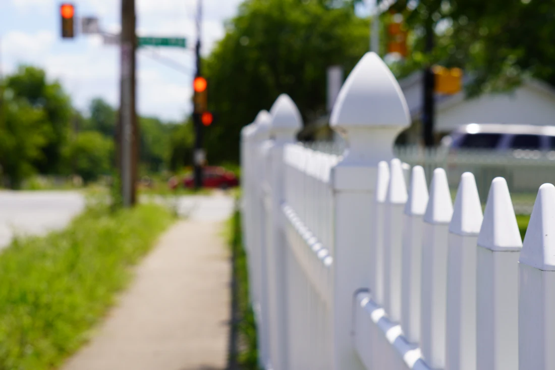 White vinyl picket fence with post caps along a sidewalk