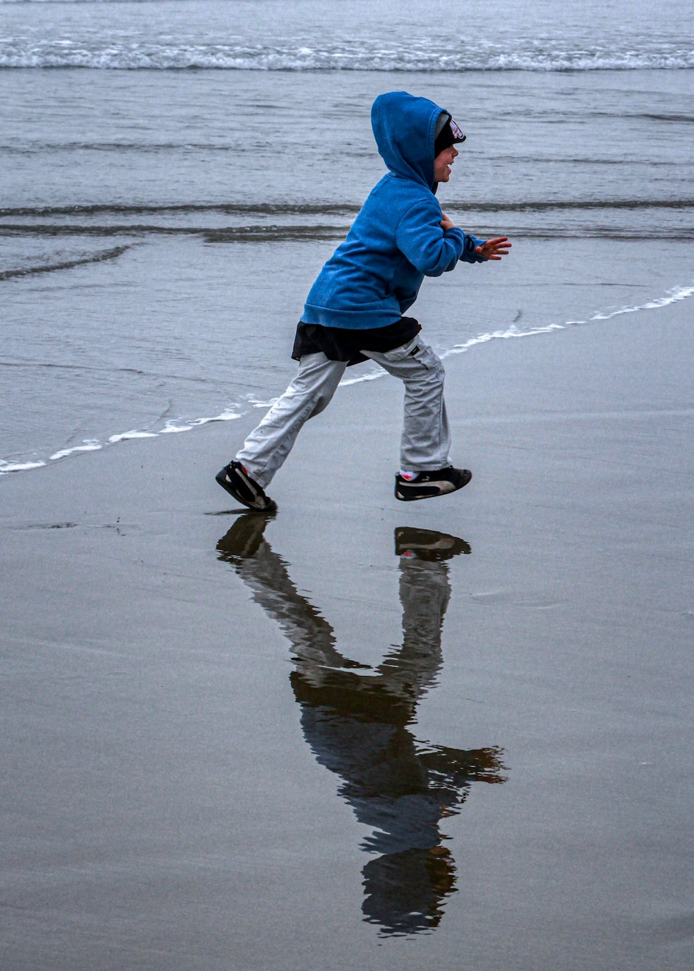 Hombre con chaqueta azul y pantalones blancos caminando sobre arena mojada durante el día