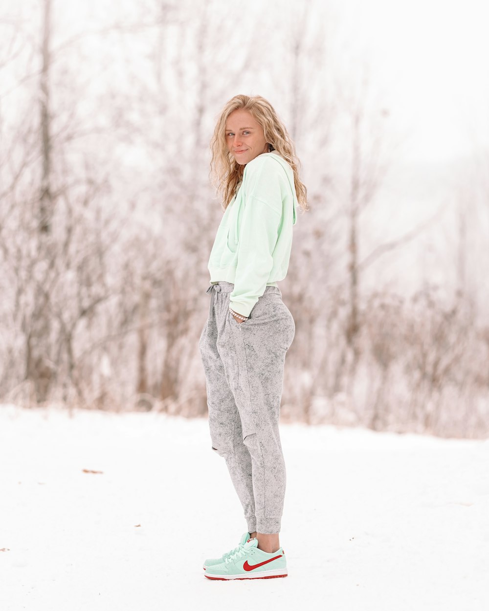 woman in white long sleeve shirt and gray pants standing on snow covered ground during daytime
