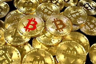 A large pile of shiny gold coins with the Bitcoin symbol embossed on them, with one coin featuring the symbol in red.