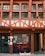 A traditional half-timbered building with an earthy color scheme of red and cream. The facade features large windows with green frames and a sign with the words 'Magasin Bio'. The lower part of the building displays window art with floral and plant motifs, incorporating orange and black tones.
