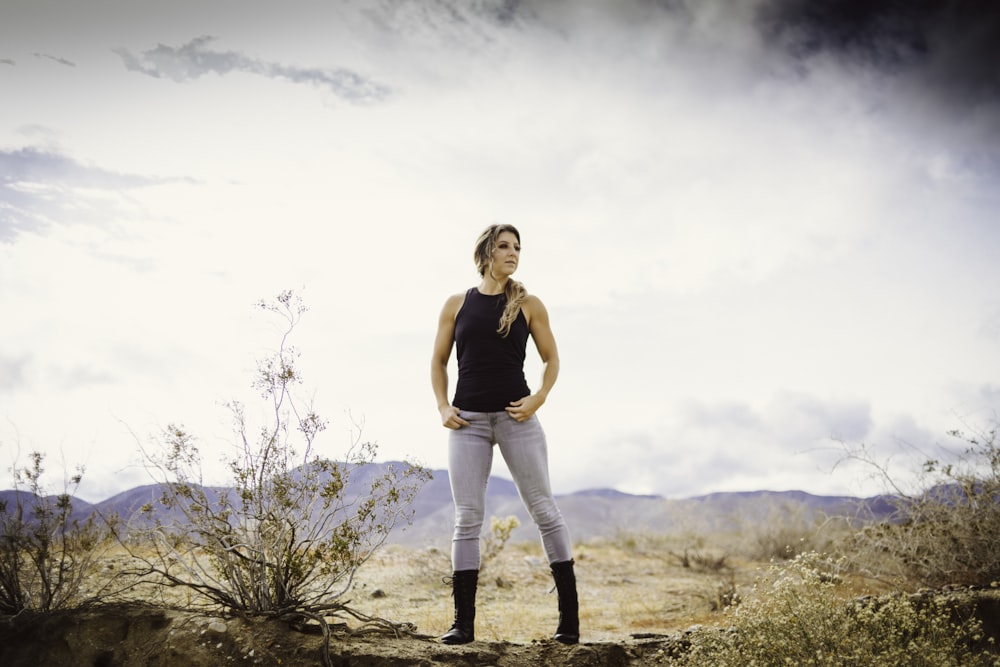 woman in black tank top and white pants standing on brown field during daytime