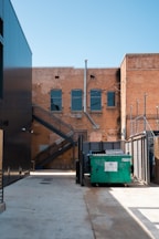 green trash bin beside brown building