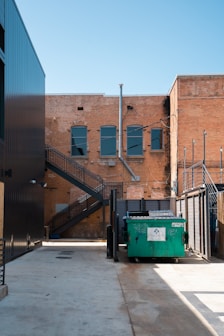 green trash bin beside brown building