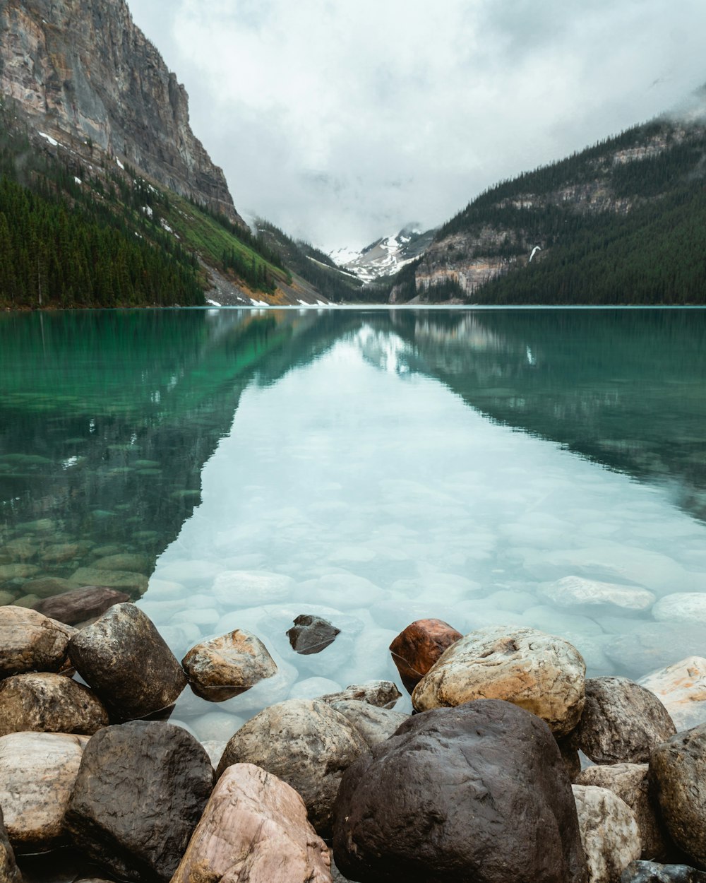 gray rocky shore near green lake and mountains during daytime