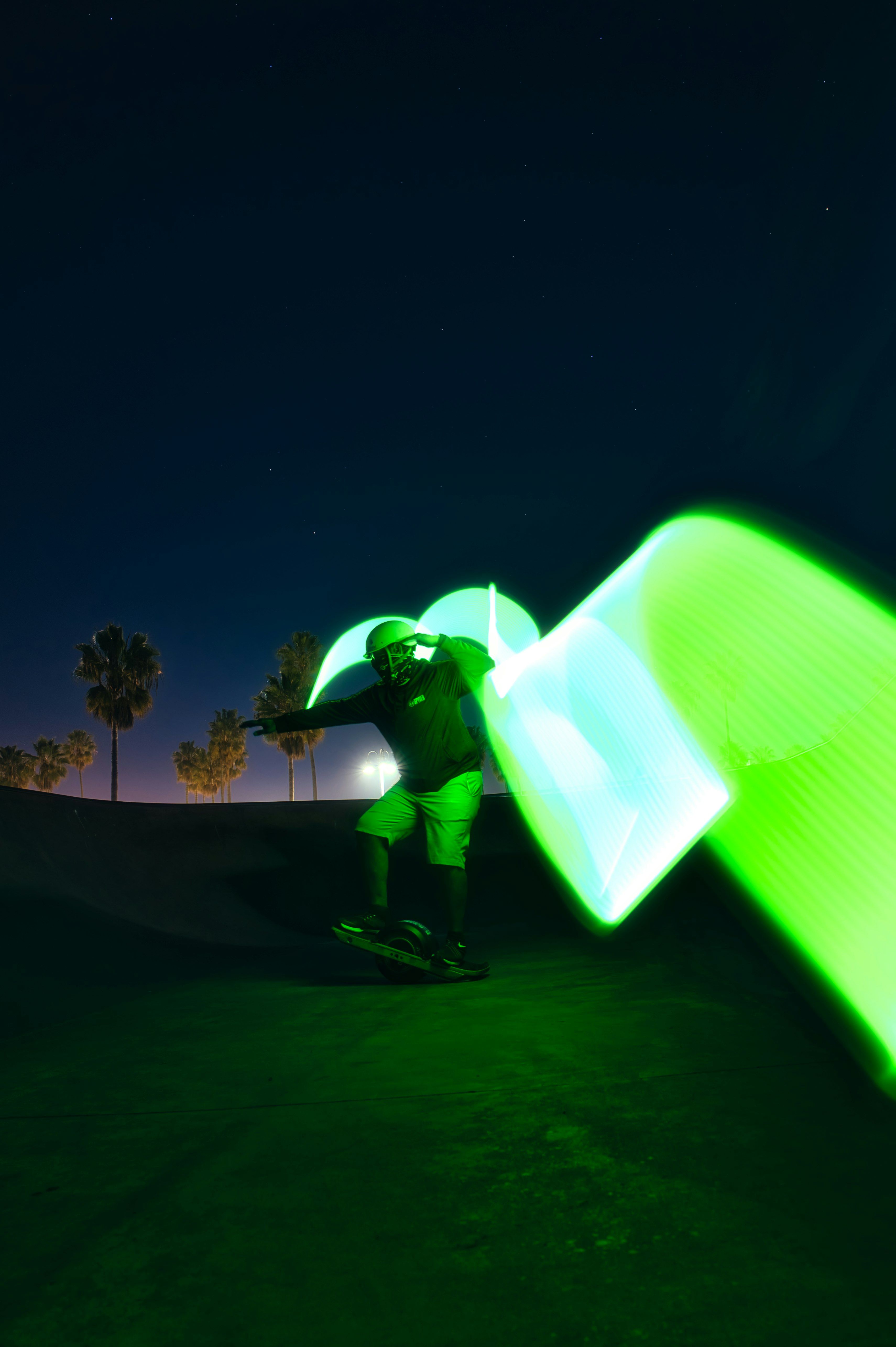 Man rides a Onewheel at night surrounded by green light. 