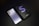 A sleek smartphone with a metallic finish lies beside its black box. The box features a large letter 'S' with the model name 'S21+ 5G' printed on it. The phone has a triple camera setup on the back and a minimalist design with the brand name visible.