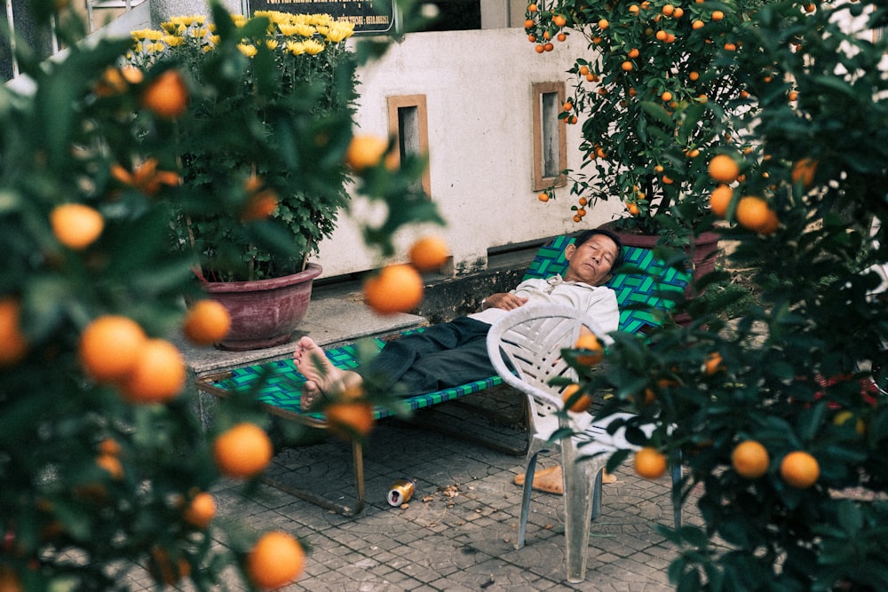 woman in white and green long sleeve shirt sitting on white metal chair near orange fruits