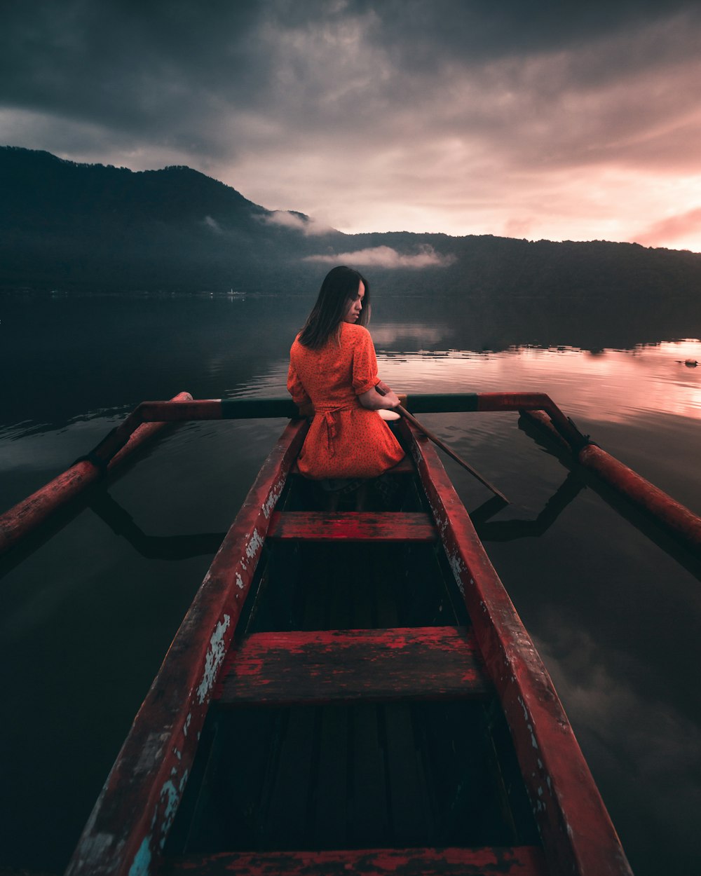 woman in red dress sitting on brown wooden dock during daytime