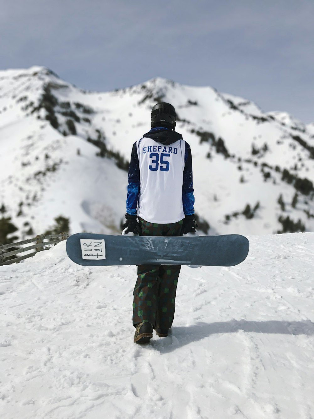 man in white and blue jacket and green pants standing on snow covered ground during daytime