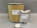 A large cardboard cylinder and a silver foil bag, both labeled with 'CMOAPI' branding, are displayed. The labels include product details such as name, CAS number, weight, and a QR code. In front of them, a small glass dish contains a white powder with a metal spoon inside.