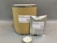 A large cardboard cylinder and a silver foil bag, both labeled with 'CMOAPI' branding, are displayed. The labels include product details such as name, CAS number, weight, and a QR code. In front of them, a small glass dish contains a white powder with a metal spoon inside.