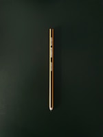 A single yellow and black pencil is placed vertically against a dark green background. The pencil is centered in the image and is sharpened to a point at the bottom. It features branding text and details printed along its side.