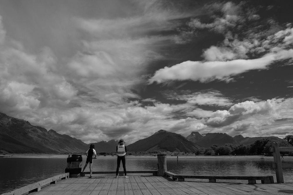 grayscale photo of 2 people walking on wooden dock