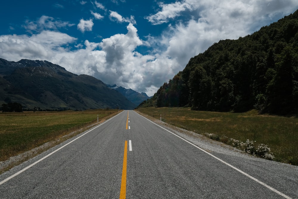 gray concrete road between green grass field under blue and white cloudy sky during daytime