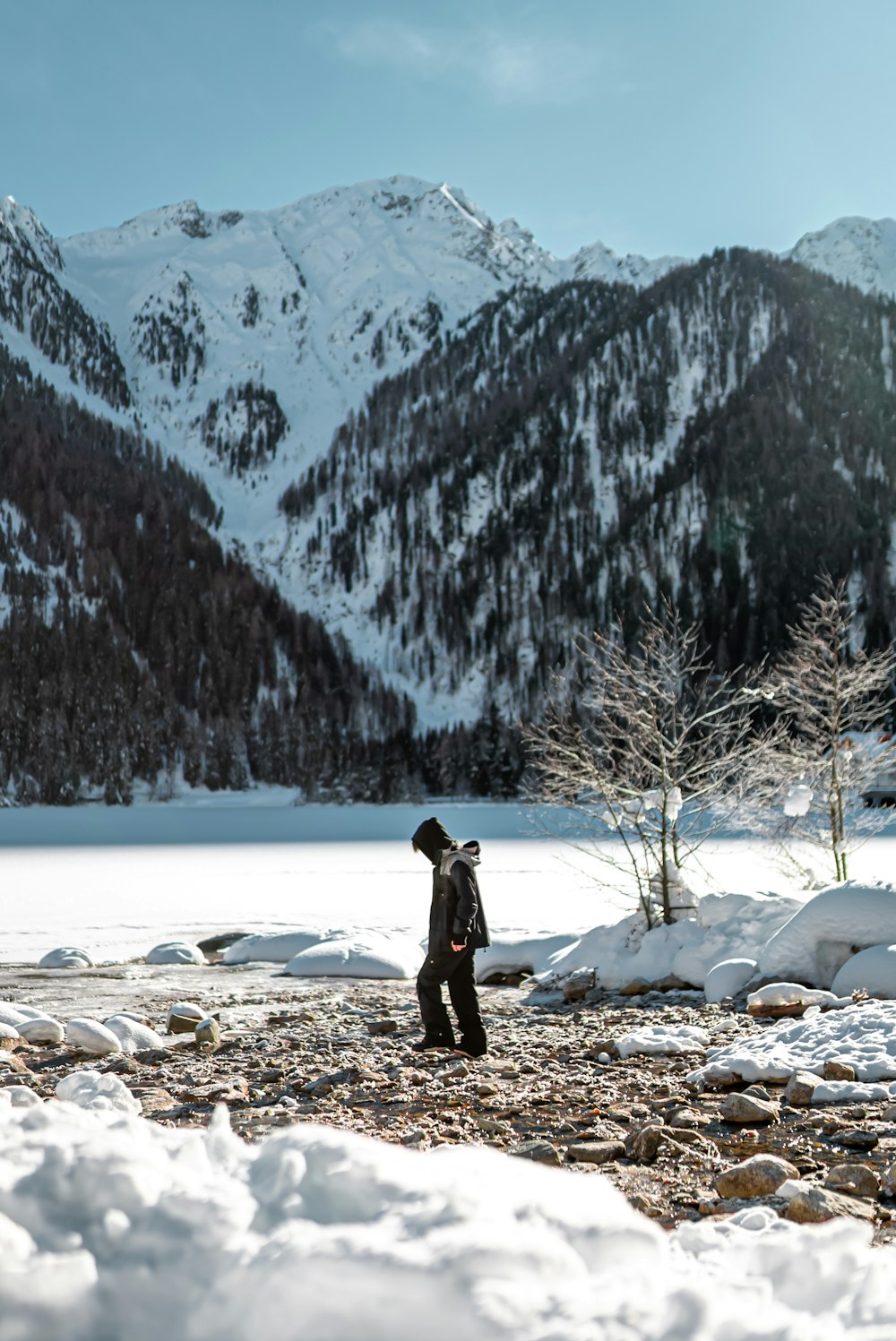 woman in black jacket standing on rocky ground near snow covered mountain during daytime