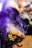 A piece of wood is partially burnt with wisps of smoke rising. The wood has a rugged, textured surface and is primarily brown with some charred black areas. There is a surreal, purple-colored smoke surrounding the wood, creating an ethereal atmosphere.