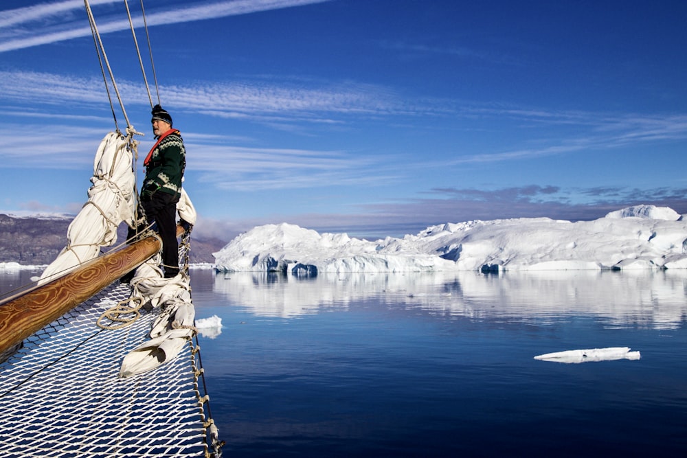 man in green jacket and blue denim jeans standing on brown wooden dock over snow covered