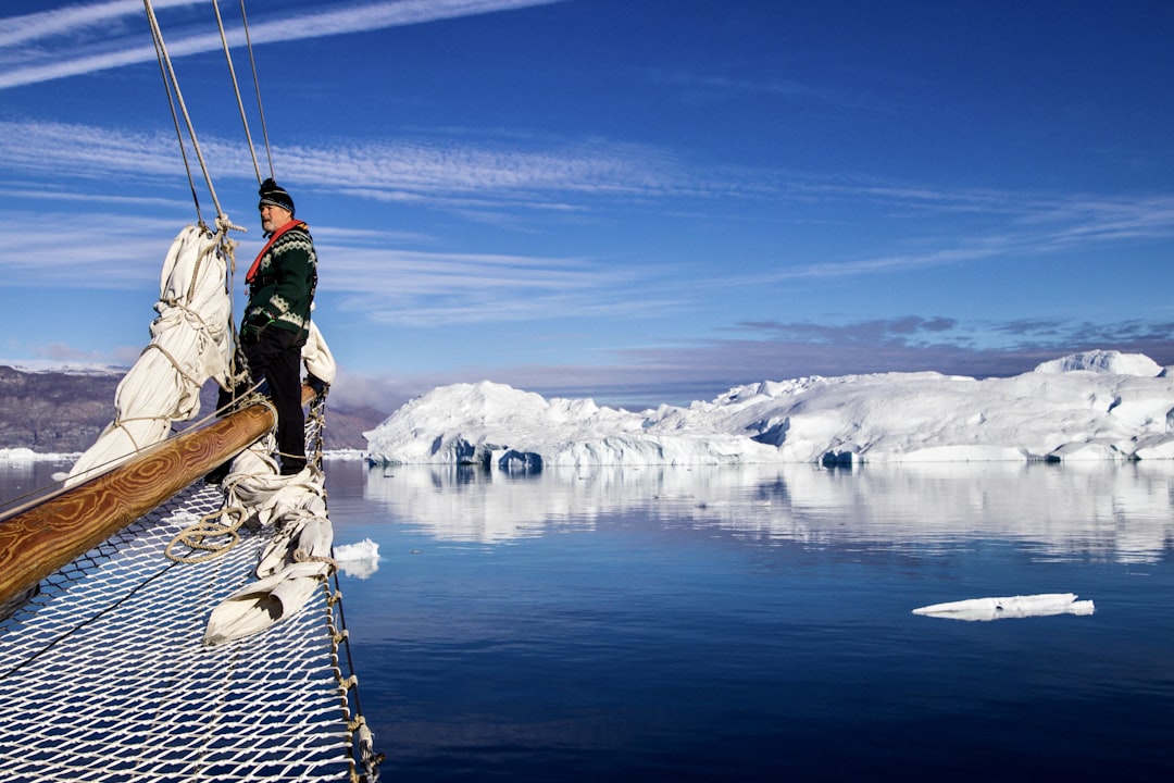 man in green jacket and blue denim jeans standing on brown wooden dock over snow covered,