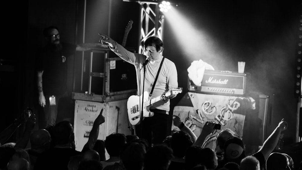 man in white dress shirt playing guitar on stage