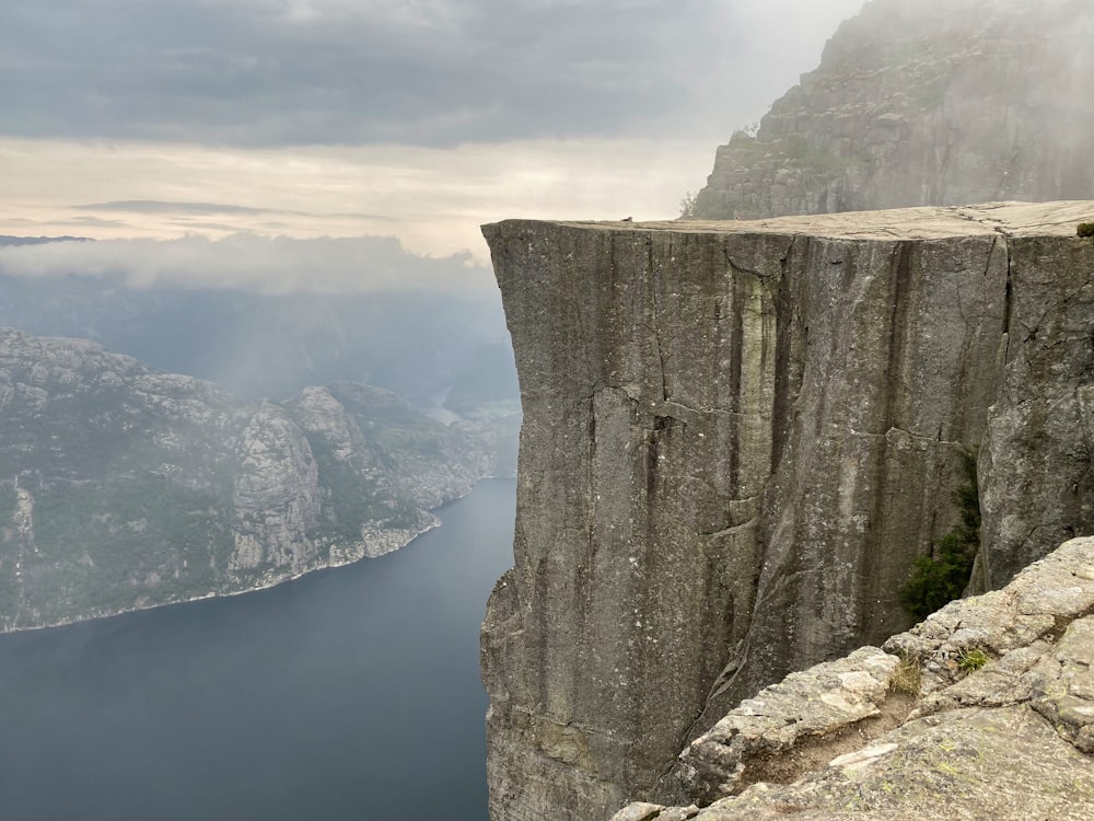 montaña rocosa gris al lado del mar azul bajo el cielo nublado blanco durante el día