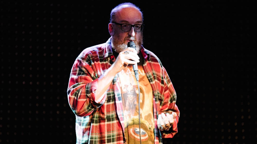 homme en chemise boutonnée à carreaux rouge et blanc tenant un microphone