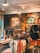A rustic store interior with wooden walls and stylish lighting. The wall features artistic graphics and text. Clothing items such as t-shirts and hats are neatly displayed on racks. The atmosphere feels laid-back and trendy.