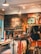 A rustic store interior with wooden walls and stylish lighting. The wall features artistic graphics and text. Clothing items such as t-shirts and hats are neatly displayed on racks. The atmosphere feels laid-back and trendy.