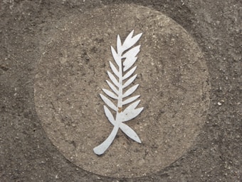 A stylized, metallic laurel branch inlaid into a textured concrete surface within a circular border.